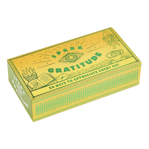 Yellow matchbox with green text "Spark Gratitude" and illustrations of a sun, open book, plant, and teacup. Text reads "50 Ways to Appreciate Every Day."