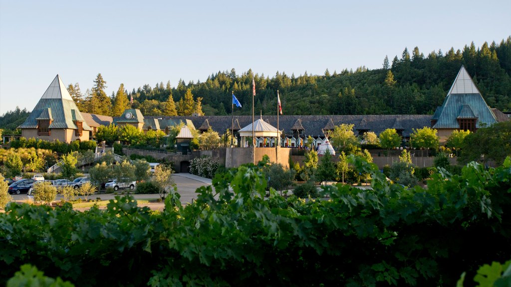 A grand building with peaked roofs surrounded by lush greenery and vineyards under a clear blue sky, evoking a serene and elegant atmosphere.