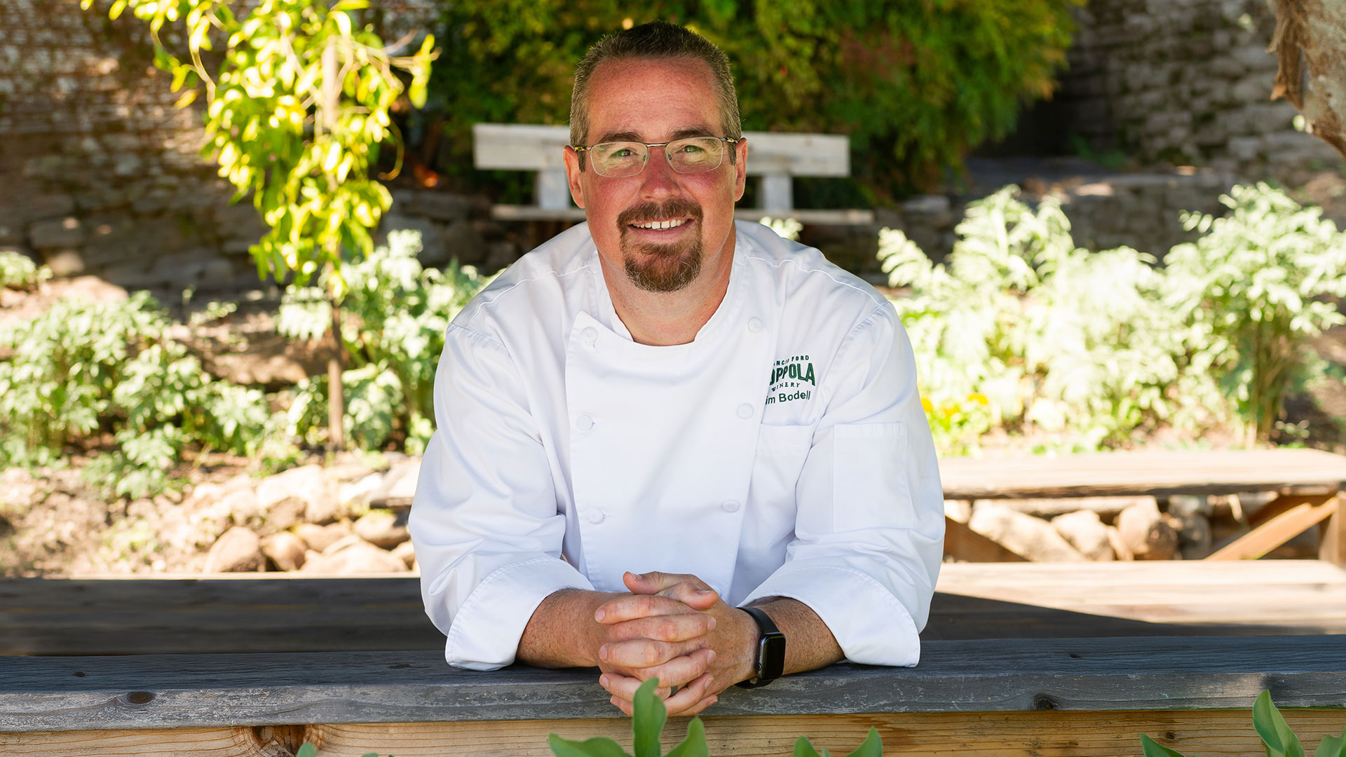 Chef Time Bodell pictured outdoors leaning on a picnic table under an umbrella