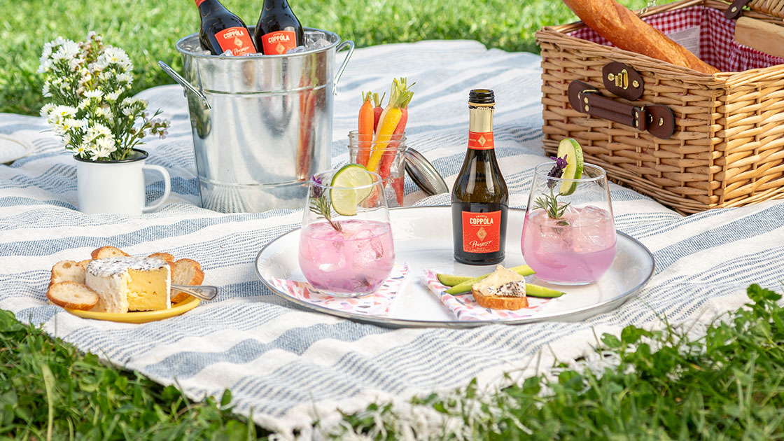 A mini bottle of Coppola Diamond Prosecco pictured with various picnic type elements on a blanket outdoors